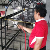Technician spraying bed bug treatment on metal bunk bed frames in a dormitory